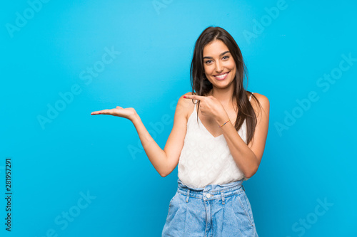 Young woman over isolated blue background holding copyspace imaginary on the palm to insert an ad