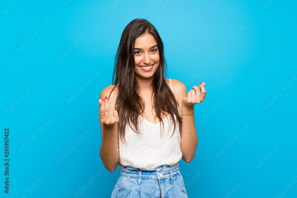 Fototapeta premium Young woman over isolated blue background making money gesture