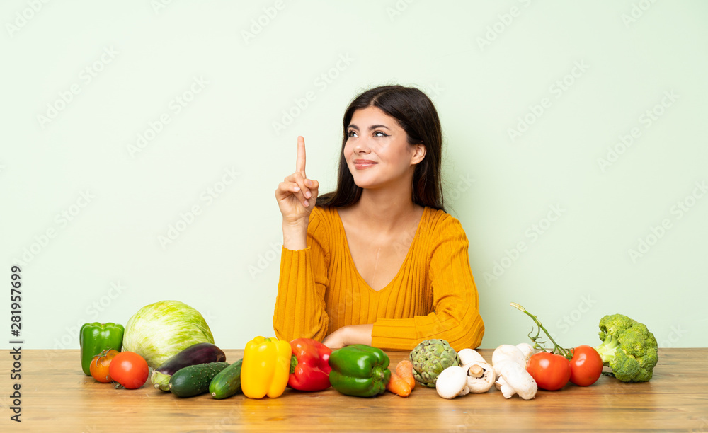 Teenager girl with many vegetables showing and lifting a finger in sign of the best Teenager girl with many vegetables showing and lifting a finger in sign of the best