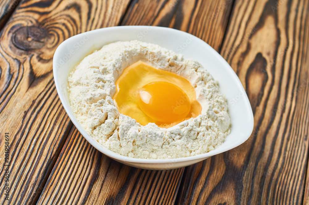 Broken egg in ceramic bowl with flour lies on rustic wooden table Broken egg in ceramic bowl with flour lies on rustic wooden table
