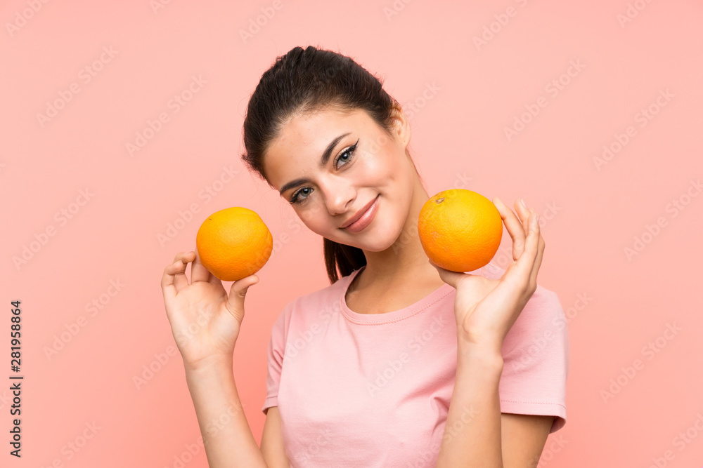 Happy Teenager girl over isolated pink wall holding oranges Happy Teenager girl over isolated pink wall holding oranges
