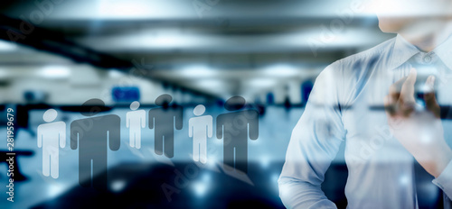 Young businessman adjusting his black colored necktie with a blurred background of office with some human shape icons on the floor concept of opportunities and employment.