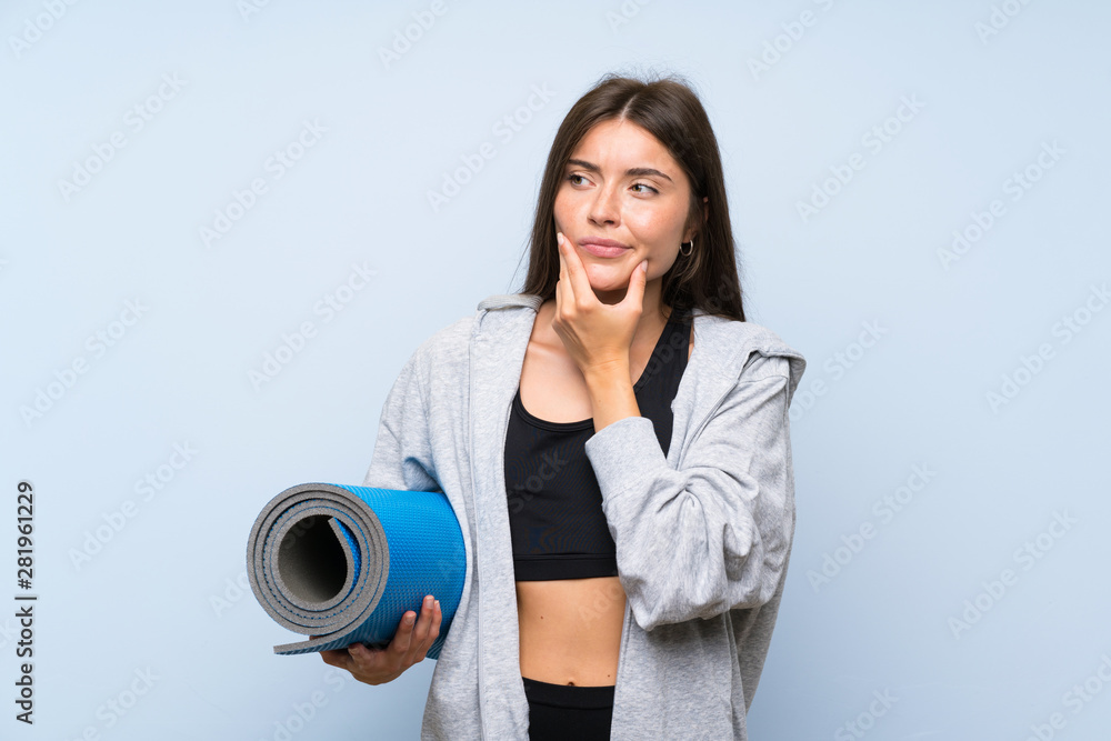 Fototapeta premium Young sport girl with mat over isolated blue background thinking an idea