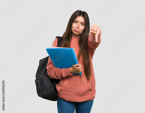 Young student woman holding notebooks showing thumb down with negative expression over isolated grey background