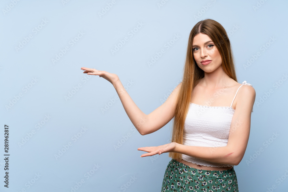 Young woman over isolated blue background extending hands to the side for inviting to come Young woman over isolated blue background extending hands to the side for inviting to come