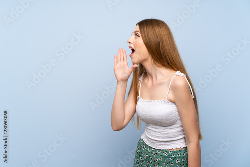 Young woman over isolated blue background shouting with mouth wide open to the lateral