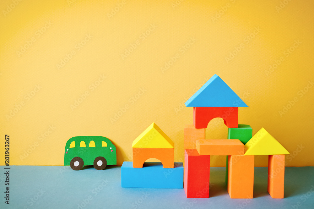 Cars cut out of paper and houses from cubes on a yellow background. Educational toys for preschool indoor playground