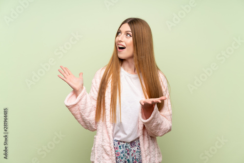 Young woman in dressing gown over green wall with surprise facial expression