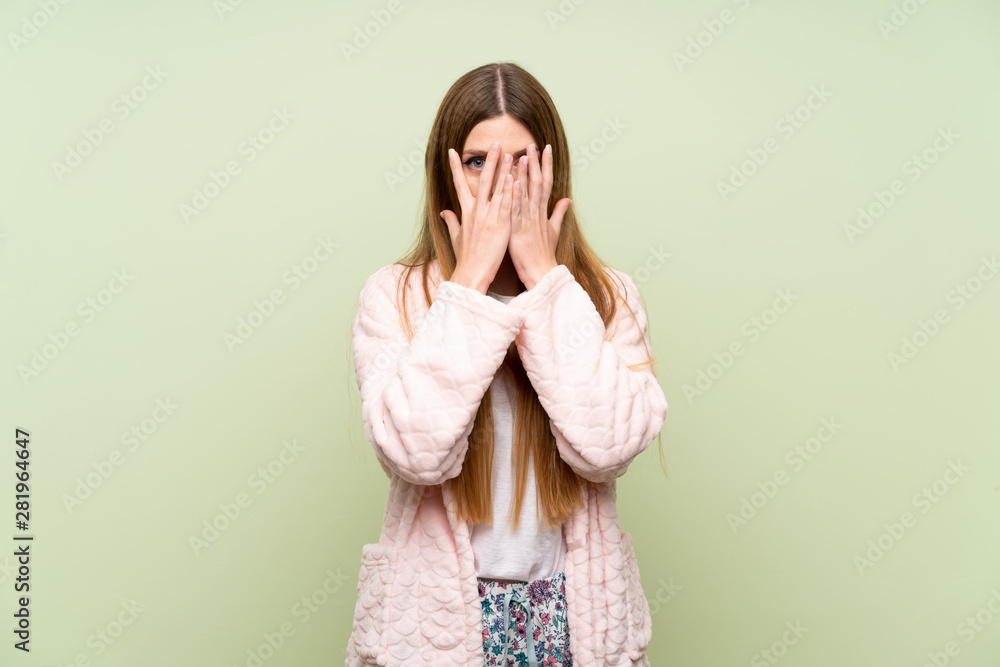 Young woman in dressing gown over green wall covering eyes and looking through fingers Young woman in dressing gown over green wall covering eyes and looking through fingers