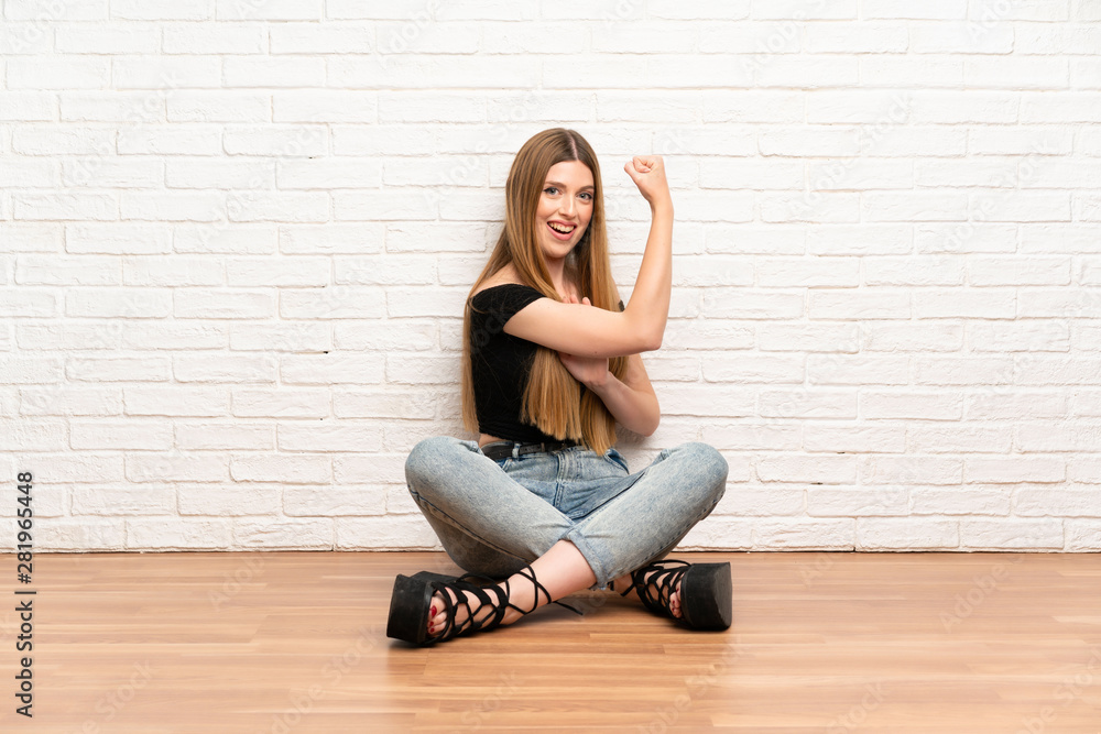 Young woman sitting on the floor making strong gesture