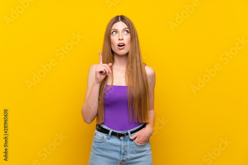 Young woman over isolated yellow background thinking an idea pointing the finger up