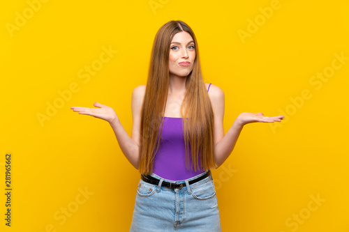 Young woman over isolated yellow background having doubts while raising hands