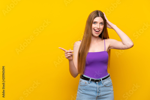 Young woman over isolated yellow background surprised and pointing finger to the side © luismolinero