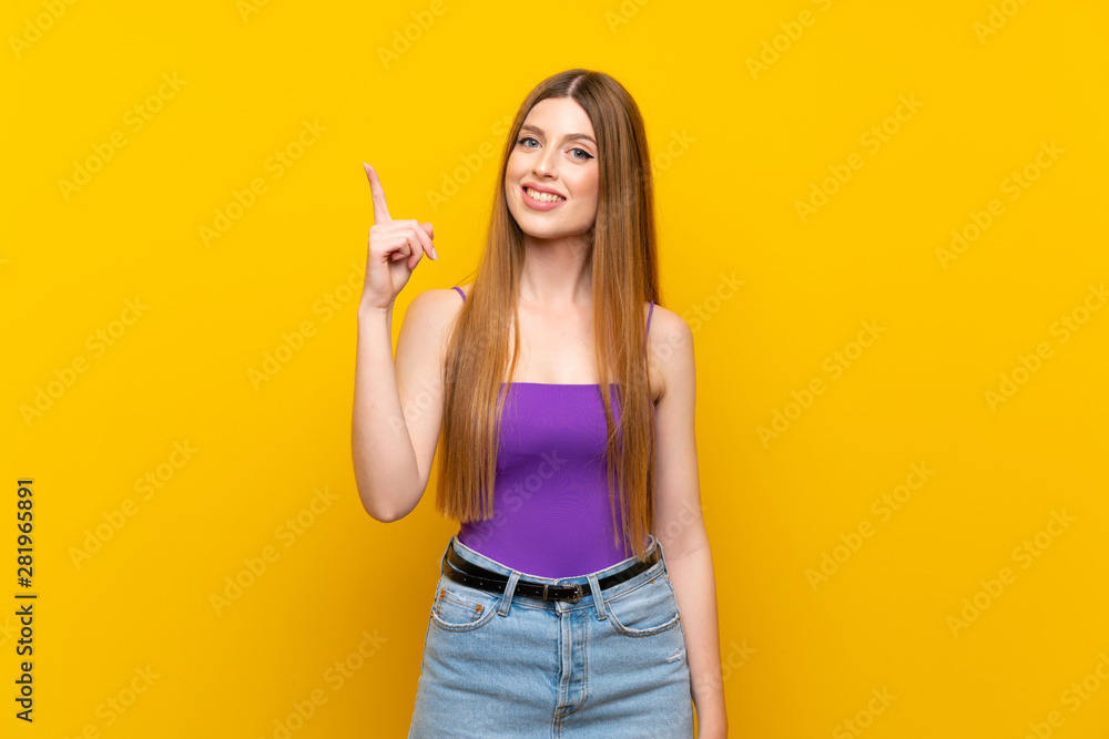 Young woman over isolated yellow background showing and lifting a finger in sign of the best Young woman over isolated yellow background showing and lifting a finger in sign of the best
