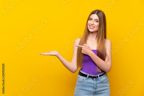 Young woman over isolated yellow background holding copyspace imaginary on the palm to insert an ad
