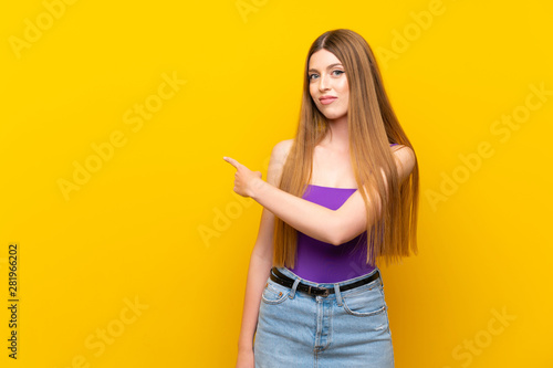 Young woman over isolated yellow background pointing back