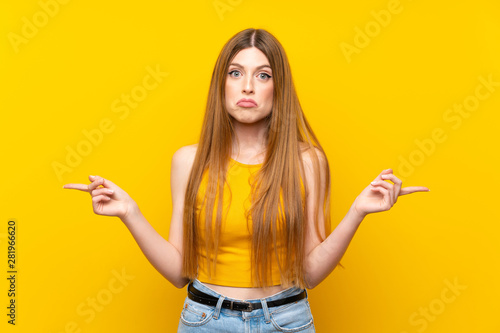 Young woman over isolated yellow background pointing to the laterals having doubts © luismolinero