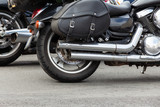 rear part of a motorcycle: wheel, exhaust pipe and black leather wardrobe trunk (luggage bag) close-up, side view