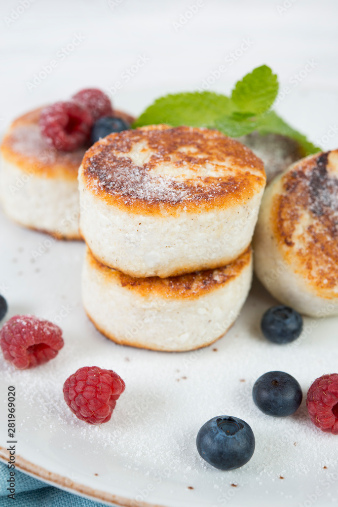 Fried curd cheesecakes decorated with fresh berries and mint. Vertical orientation.