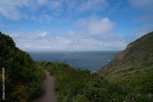 Hiking path trail with rocky cove leading to ocean and blue skies