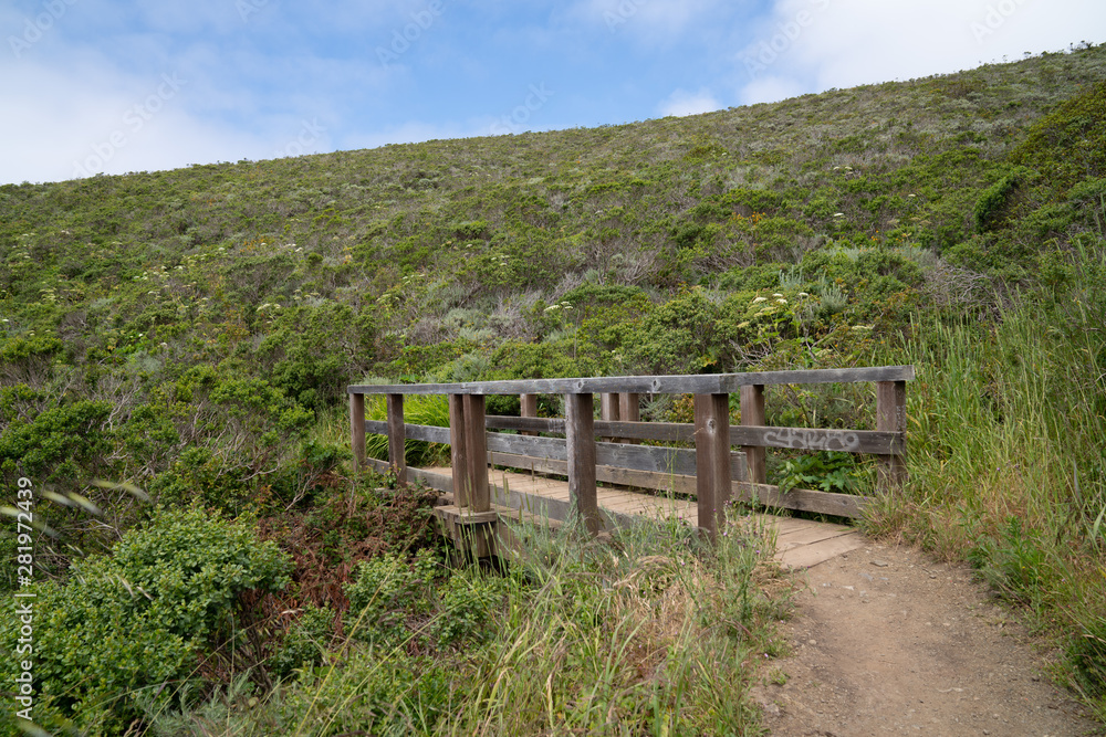 Small wooden bridge on dirt trail path below large hill