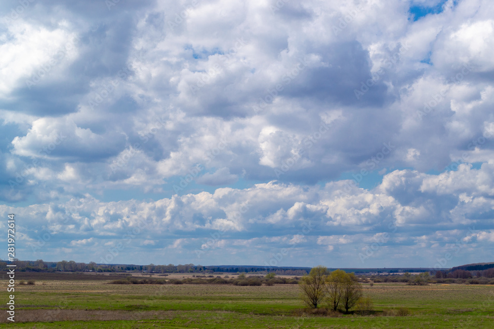 Massive cumulus white clouds in a blue sky over a green plain.