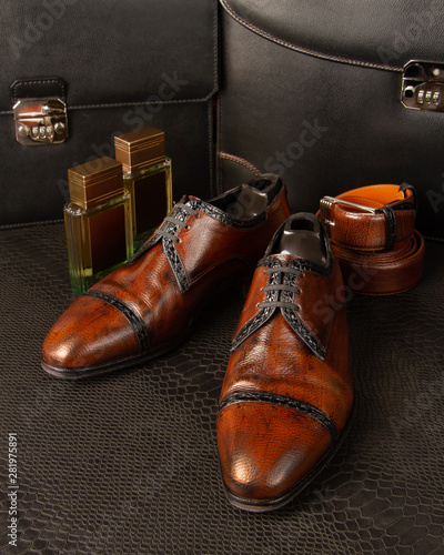 Composition of a pair of men's brown shoes, two bottles of men's fragrance and men's trouser belt against the background of men's briefcases © storyteller63