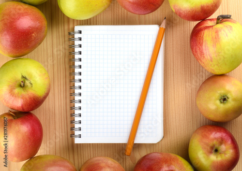 Squared paper notebook on wooden table top view. Ripe apples around the notebook.