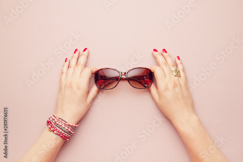 Top view of trendy sunglasses over the pink pastel background hold by woman hands
