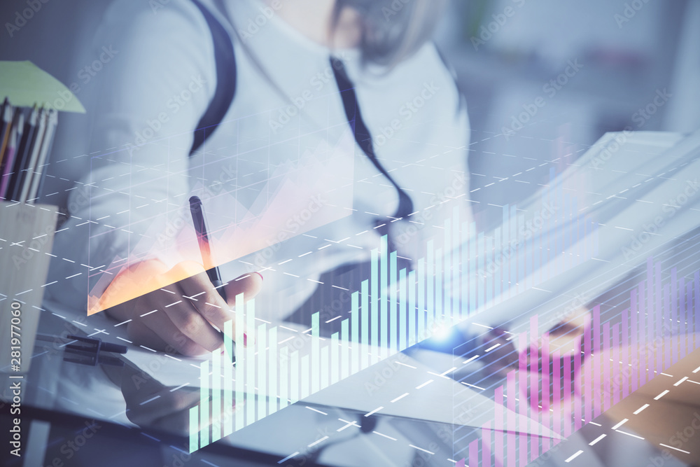 A woman hands writing information about stock market in notepad. Forex chart holograms in front. Concept of research. A woman hands writing information about stock market in notepad. Forex chart holograms in front. Concept of research.