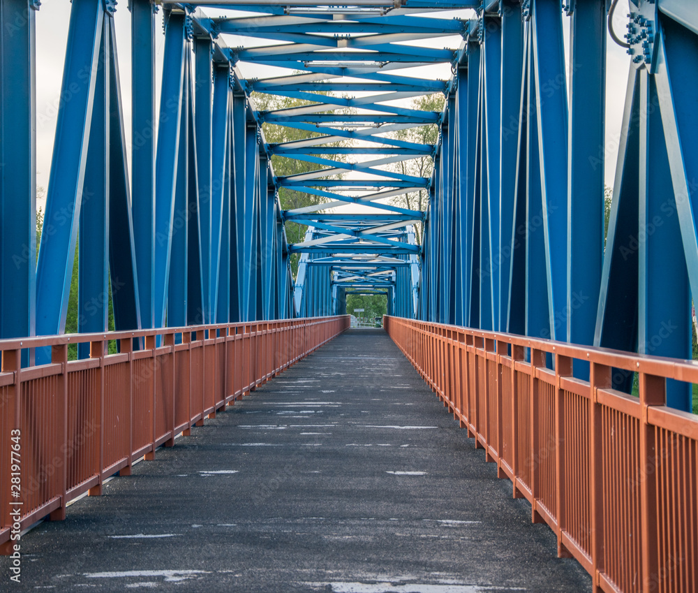 Metallic blue pedestrian bridge construction with orange railing and wooden coating close-up.