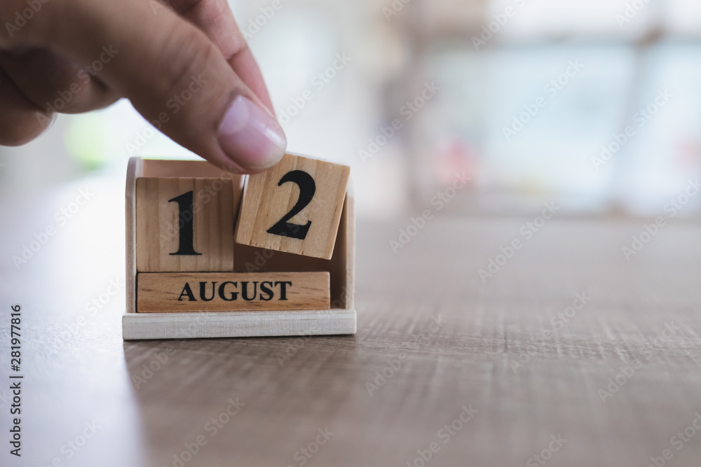 Mother's Day in Thailand, August 12, close up of left hand is picking up a wooden calendar block that is placed on a wooden table and copy space Mother's Day in Thailand, August 12, close up of left hand is picking up a wooden calendar block that is placed on a wooden table and copy space