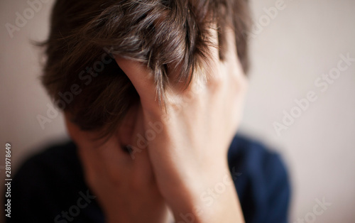 Teen boy covers his face with his hands photo