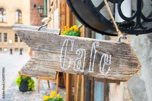 Word coffee written on an arrow-shaped wooden base, old style, retro, with old buildings and flowers on background, Riga old town