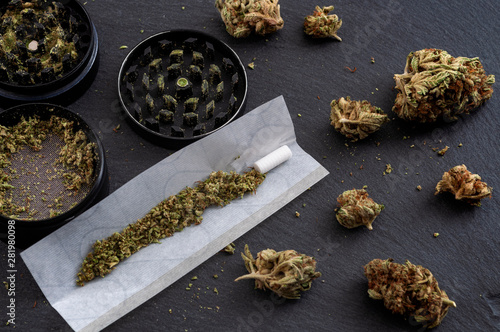 Preparing a joint and drug paraphernalia concept theme with herb girder used to grind cannabis buds and roll marijuana joints, next to rolling paper and weed bud isolated on dark background photo