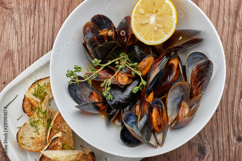 Mussels on a white plate on a wooden board
