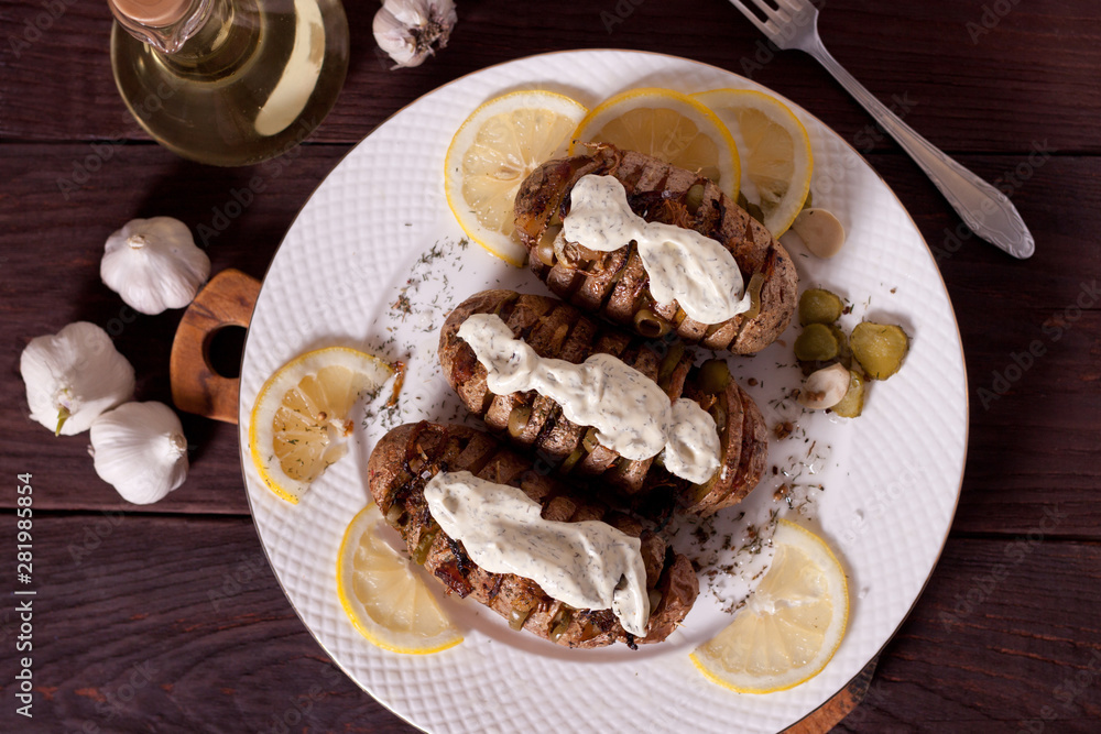 Baked potato with onions and spices on a white dish on the background of a wooden table Baked potato with onions and spices on a white dish on the background of a wooden table
