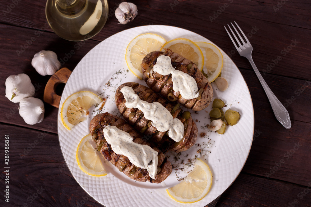 Baked potato with onions and spices on a white dish on the background of a wooden table Baked potato with onions and spices on a white dish on the background of a wooden table