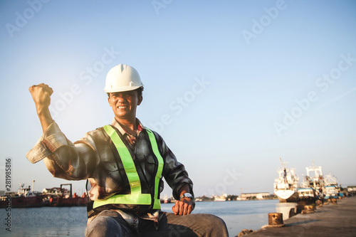 The male engineer worked at the pier, wearing a white hat, raising both hands, strong and powerful to continue working.