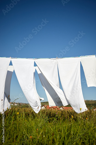 clean white clothes hanging on a rope moved by the wind in green meadow