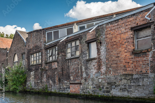 Gent, Flanders, Belgium -  June 21, 2019: Old red-brown brick industrial warehouses along the Lieve River under blue sky with white cloud patches. Greenish water. photo