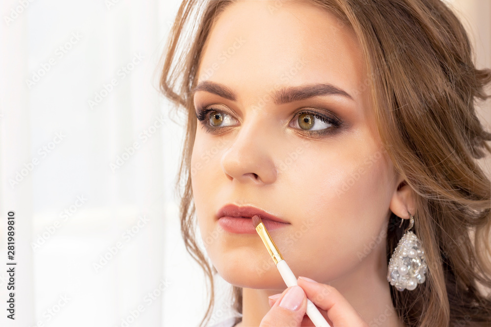 Makeup artist applies makeup to the model. lip paint brush for lipstick. beautiful girl model, portrait. Nude colors in makeup. wedding, evening makeup. Makeup artist applies makeup to the model. lip paint brush for lipstick. beautiful girl model, portrait. Nude colors in makeup. wedding, evening makeup.