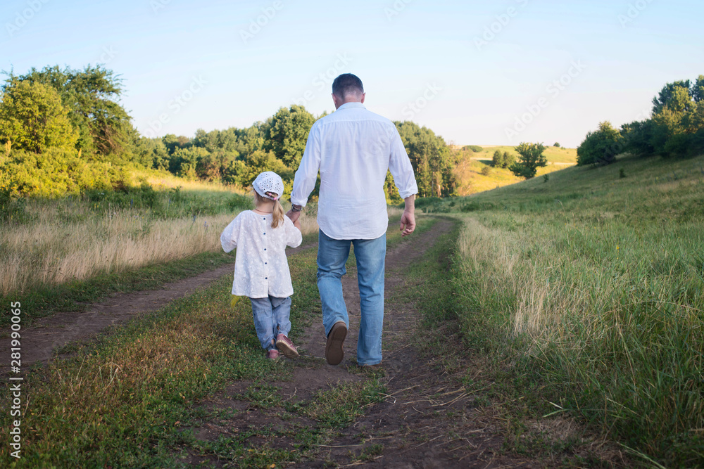 Back view of mature father and little girl daughter enjoy their walk in nature. Parenthood, fatherhood, adoption, family and people concept. Precious family moments outdoors.