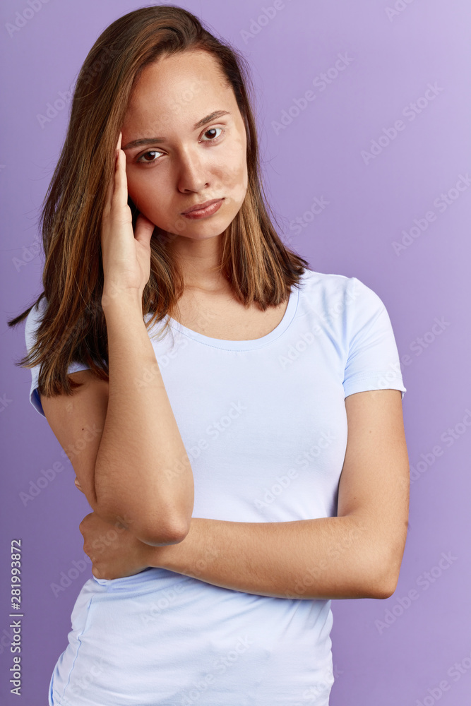 unhappy girl touching her temple, thinking about methods of removing spots on her face. close up portrait. isolated blue background unhappy girl touching her temple, thinking about methods of removing spots on her face. close up portrait. isolated blue background