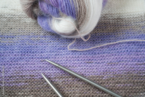 Tools for needlework: knitting fabric, tangle of thread of multicolored yarn, knitting needles. Purple, brown, white, beige colors of knitting project. for yarn stores, needlework, banner design.