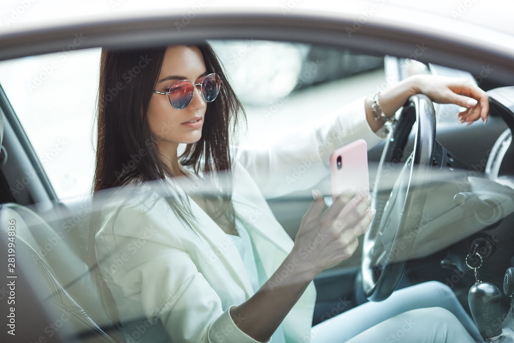 Naklejka premium Attractive young woman driving a car. Fancy woman in the automobile. Rich adult female in the car. Confident woman.