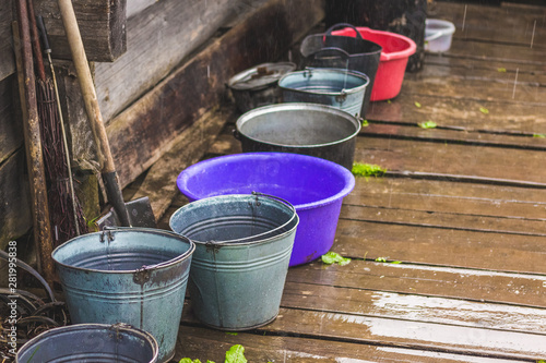 Agricultural equipment under the house in rainy weather. Bucket and bowl on a wood floor_