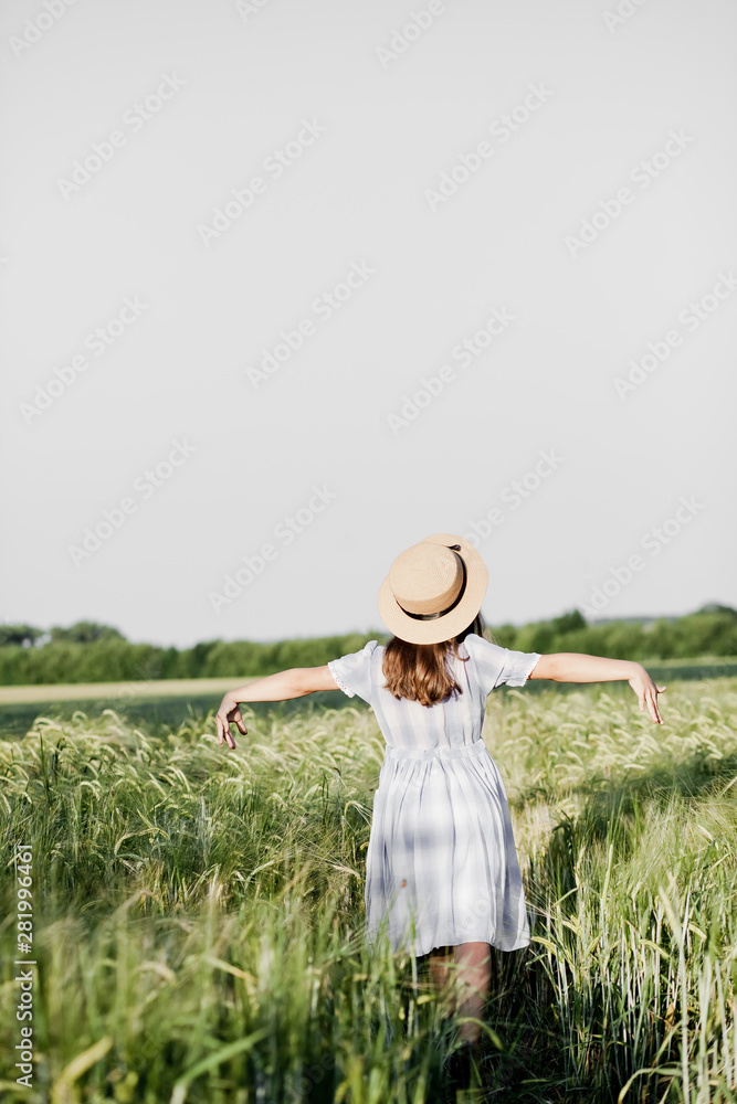 A cheerful girl in a hat walks in a wheat field. Rejoices and dances.