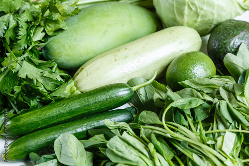 Fresh green vegetables variety on rustic white background from overhead, celery, avocado, cabbage, mango, cucumber, spinach, lime, squash. Healthy, vegetarian concept. Flat lay, top view