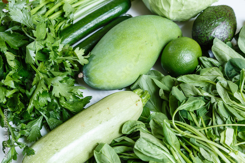 Fresh green vegetables variety on rustic white background from overhead, celery, avocado, cabbage, mango, cucumber, spinach, lime, squash. Healthy, vegetarian concept. Flat lay, top view